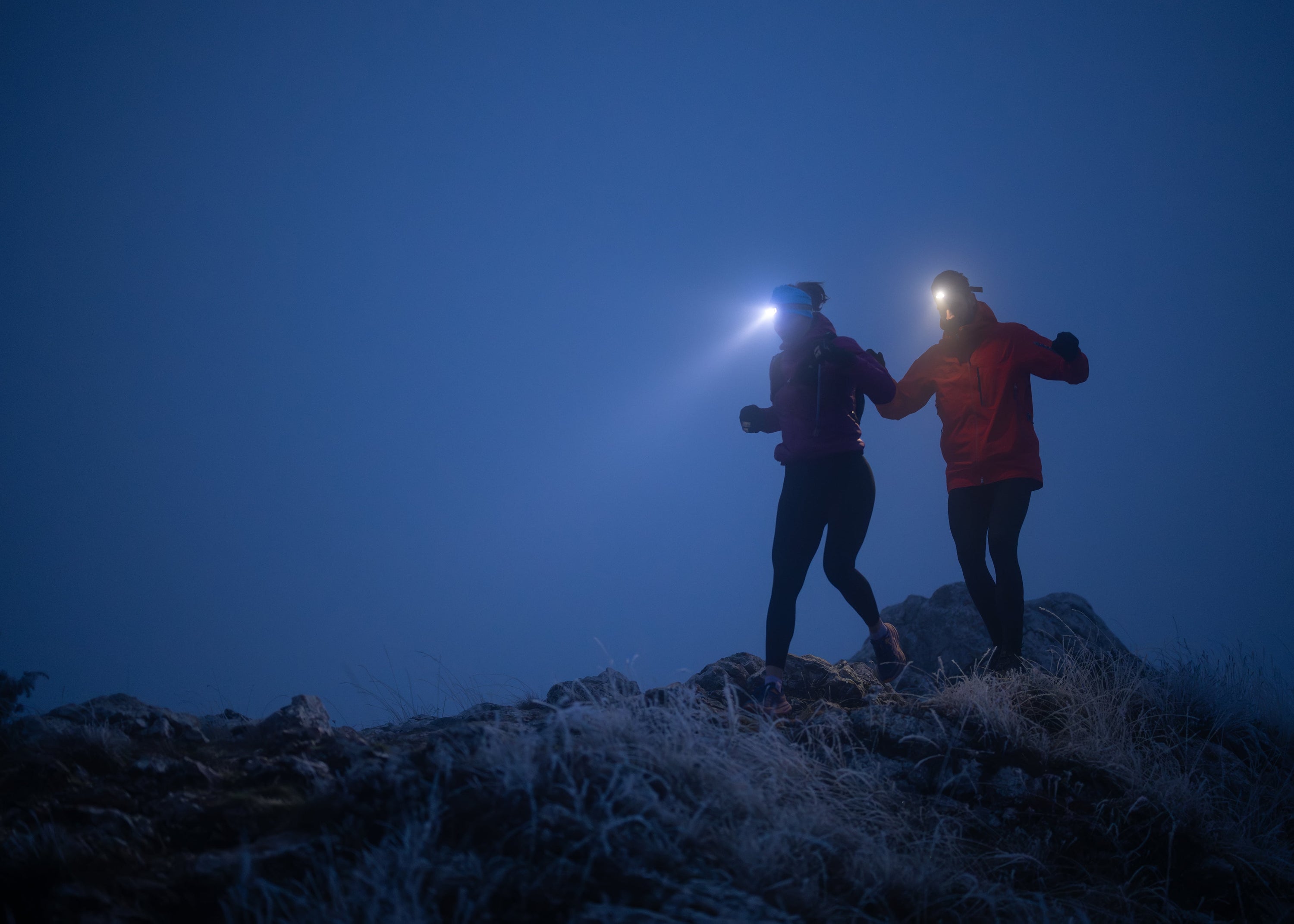 Two people on a mountain top at night with headlamps